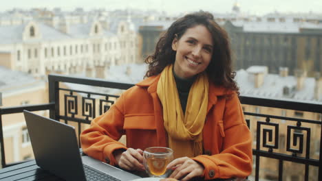 Portrait-of-Cheerful-Woman-with-Tea-and-Laptop-on-Rooftop-Terrace