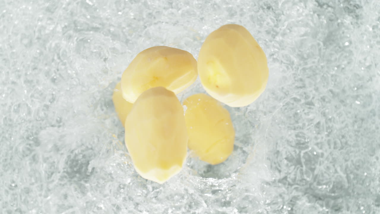 剥がされたジャガイモが沸騰する水の鍋に落ちてスローモーションでスプラッシュをしますテーブルのトップビュー