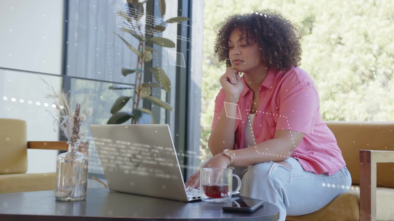 Woman leaning toward laptop, typing and pausing to read screen, reaching mug while doing tech work