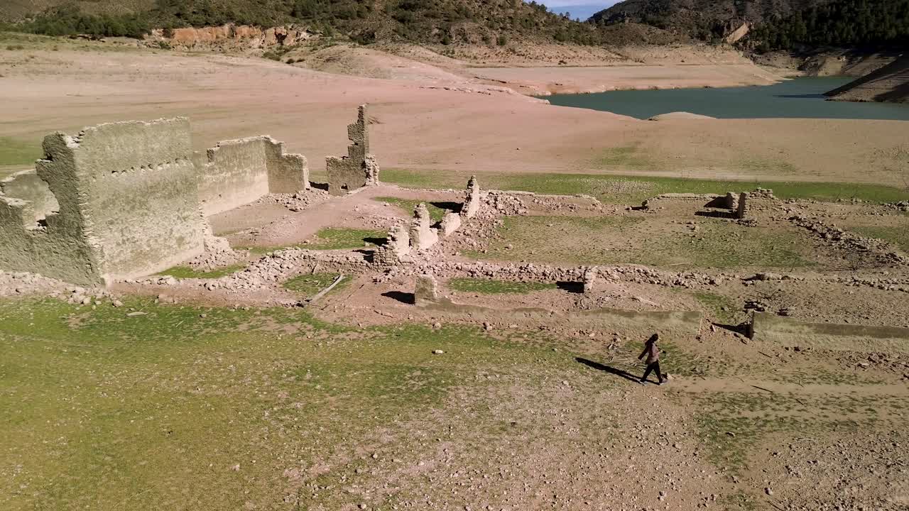 Brunette girl exploring drought-affected ruins, capturing photographs of structures exposed by low water levels at a reservoir