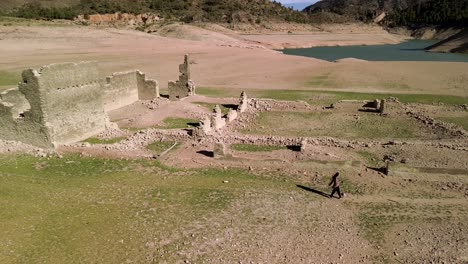 brunette girl exploring drought-affected ruins, capturing photographs of structures exposed by low water levels at a reservoir