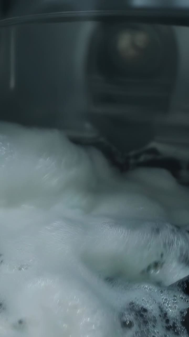 Video verticale: ondata d'acqua che fa scivolare schiuma di sapone bianca lungo la parete del lavabo, rivelando la manopola