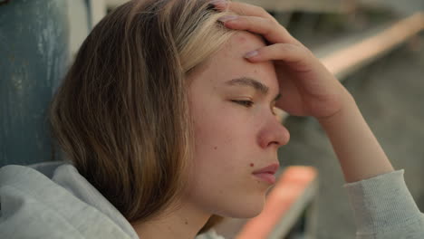 close-up of young lady gently rubbing her forehead with thoughtful expression, showcasing a moment of deep contemplation, background softly blurred