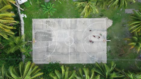 people plating basketball on court between palm trees in tropical siargao island, philippines, static high angle aerial view