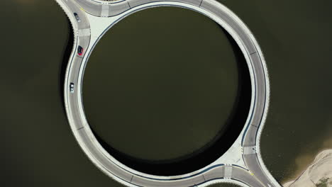 cars crossing circular bridge over laguna garzon uruguay, bird's eye drone rotate