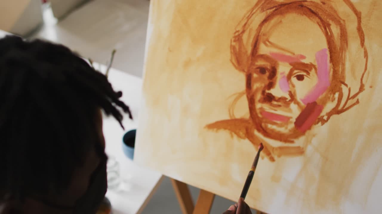 African american male artist wearing face mask painting on canvas at art studio