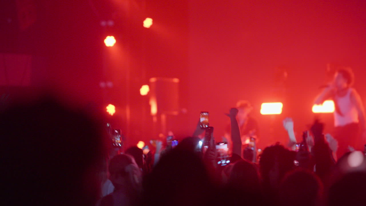 Folla a un concerto che filma gli artisti con smartphone sotto luci rosse