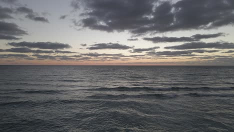 Birds-fly-through-empty-dark-dawn-beach-sunrise-aerial,-cloudy-sky