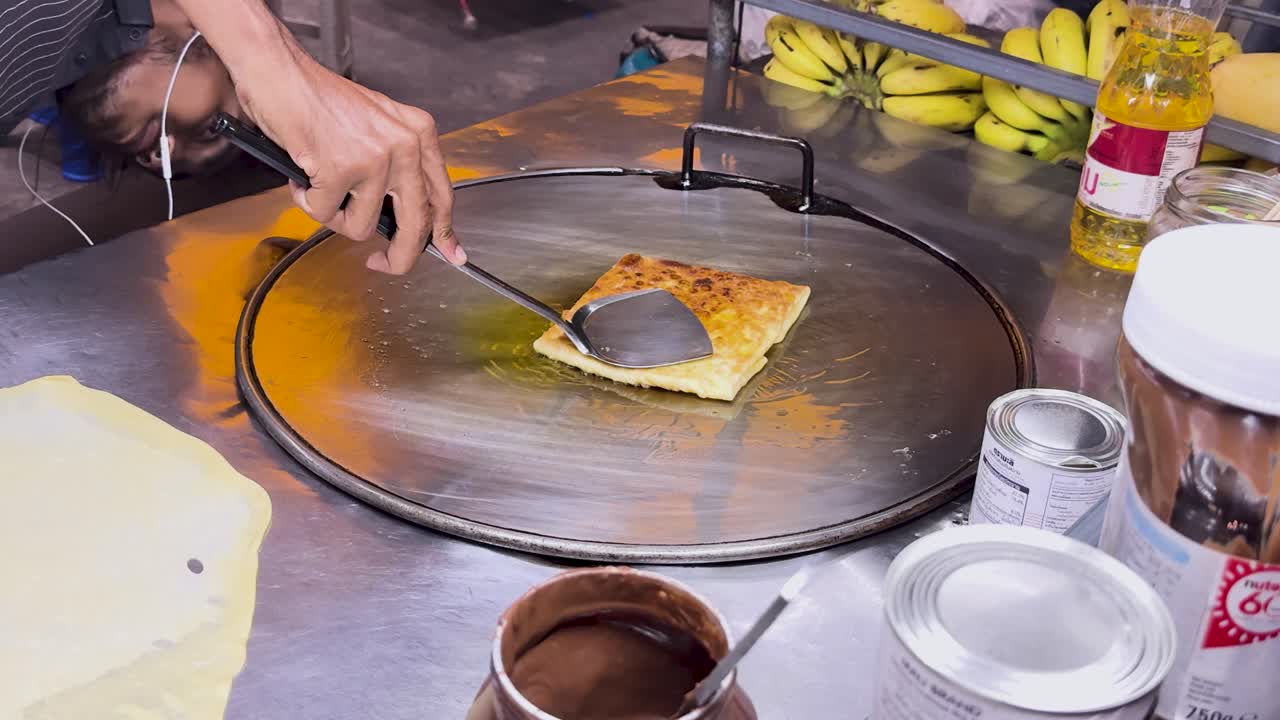 un vendedor callejero prepara hábilmente roti tailandés en una parrilla caliente en phuket, mostrando técnicas tradicionales de comida callejera