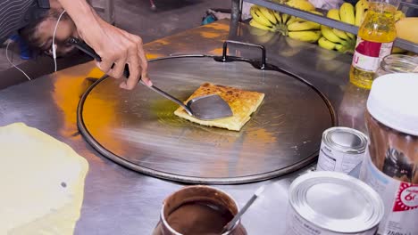 un vendedor callejero prepara hábilmente roti tailandés en una parrilla caliente en phuket, mostrando técnicas tradicionales de comida callejera