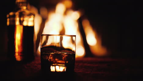 Un-Vaso-De-Whisky-Y-Una-Botella-Sobre-La-Mesa-En-El-Fondo,-Un-Fuego-Arde-En-La-Chimenea