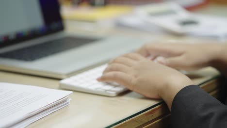 las manos de la mujer de negocios escribiendo en el teclado de la computadora portátil para buscar información, informe de investigación de marketing en el escritorio de la oficina