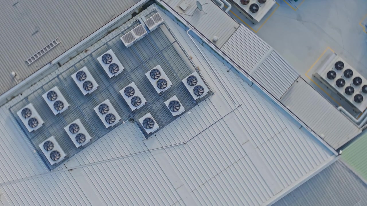 Drone shot of a modern data center rooftop featuring multiple industrial HVAC units, metallic structures, and clean geometry under daylight. Static, overhead composition highlights technology.