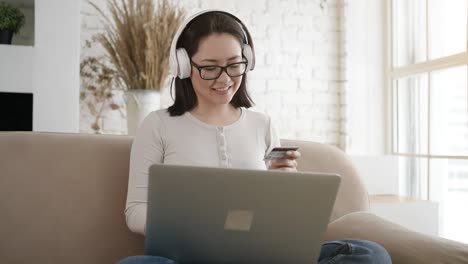 happy young asian woman doing payments online or shopping in internet store holding credit card using laptop computer