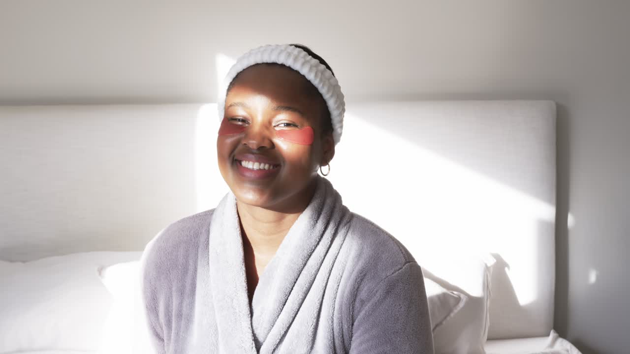 African American woman sitting on bed with eye patches smiling and looking with sunlight streaming