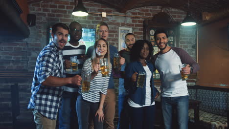 multiethnic group of friends posing to the camera with beer in hands and smiling in the pub