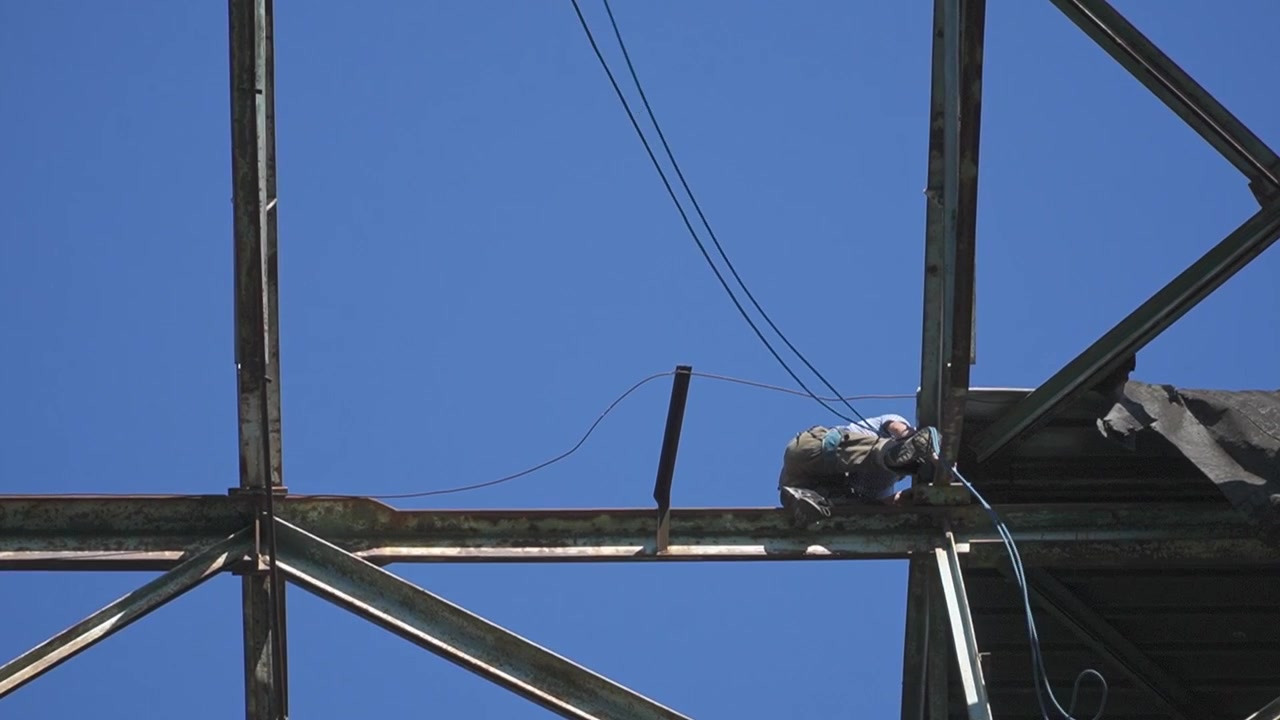 A construction worker carefully navigates a steel framework against a clear blue sky. Ideal for construction, safety, or industrial themes.