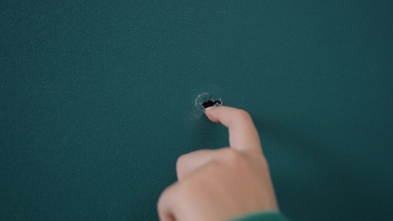 Finger poking hole in teal wall while unpacking during movein green sleeve visible as curious fingertip probes tiny opening interior apartment scene feels playful and investigative, closeup detail