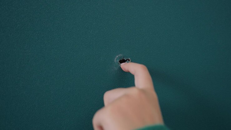 Finger poking hole in teal wall while unpacking during movein green sleeve visible as curious fingertip probes tiny opening interior apartment scene feels playful and investigative, closeup detail