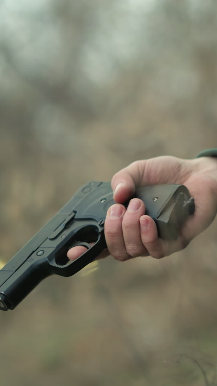 una vista cercana de un hombre mirando intensamente hacia el lado, sosteniendo una pistola, el fondo presenta un bosque, con tres bolas borrosas como luz amarilla vista