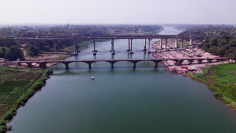 crop field lands with tilwara narmada river bridge and flying birds at narmada ghat, tilwara, jabalpur, madhya pradesh, india. day time, push in, drone shot, 4k.