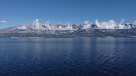 drone circles at high altitude over open water with view on croatian coast line until a sailboat comes into view sailing peacefully into the horizon