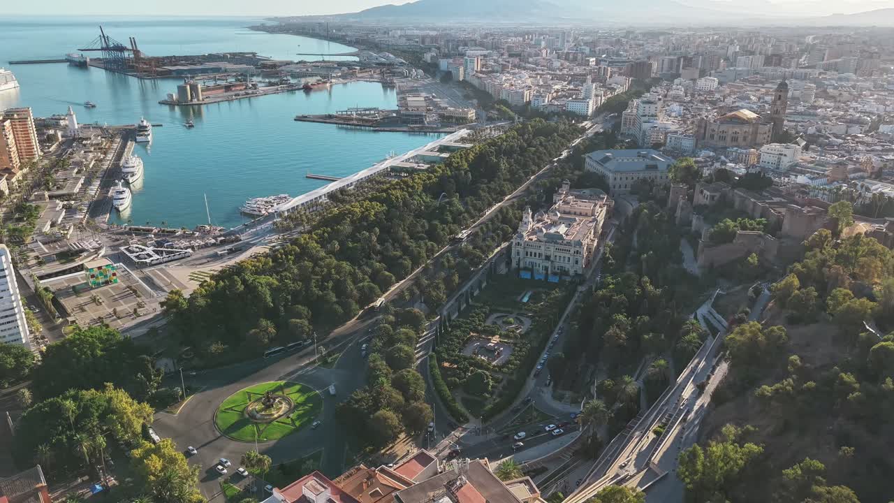 Vertical drone shot shows Málaga harbor, city center, and lush park from Gibralfaro vantage