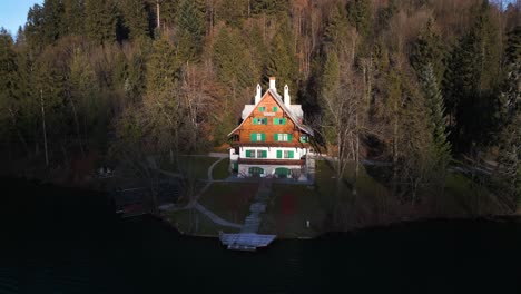 Bright-sunlit-cabin-on-top-of-hill-above-boathouse-and-dock-overlooks-serene-lake