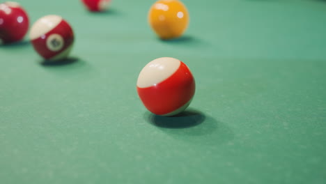 close up of hand rolling billiard ball on green pool table. focus on motion and dynamics of game as ball moves across felt surface. scattered colorful balls in background
