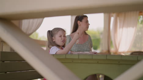 Grimacing-little-girl-eats-hot-food-near-mother-in-cafe