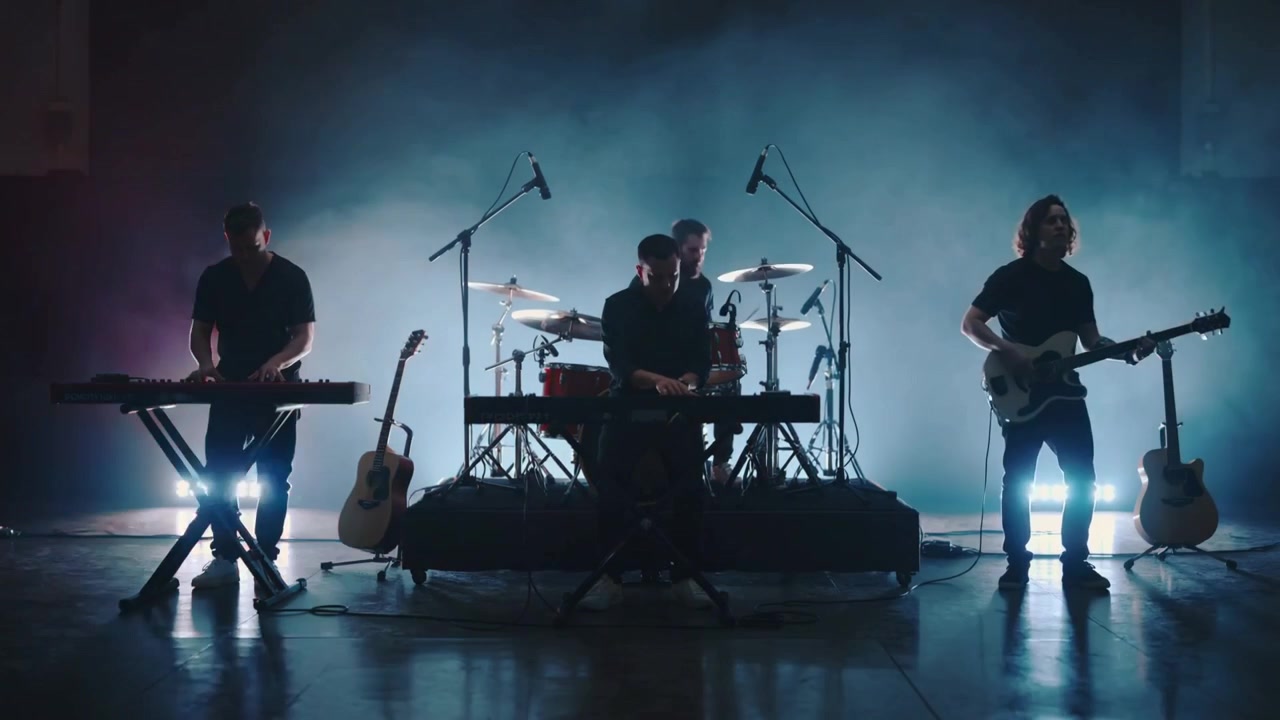 Røde uplights skifter, mens en kvartet spiller keyboards, trommer og guitar på scenen og øver.