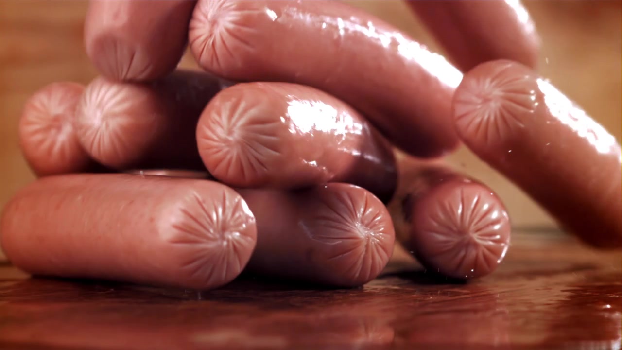 Slow motion di salsicce fresche che cadono su una superficie di legno bagnata