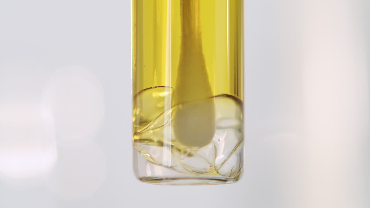Macro Shot Of Yellow Oil Base In A Tube With Bubbles At The Bottom, Stirred By A Cotton Bud