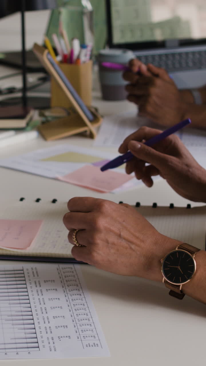 Close-up of people working and taking notes at a desk