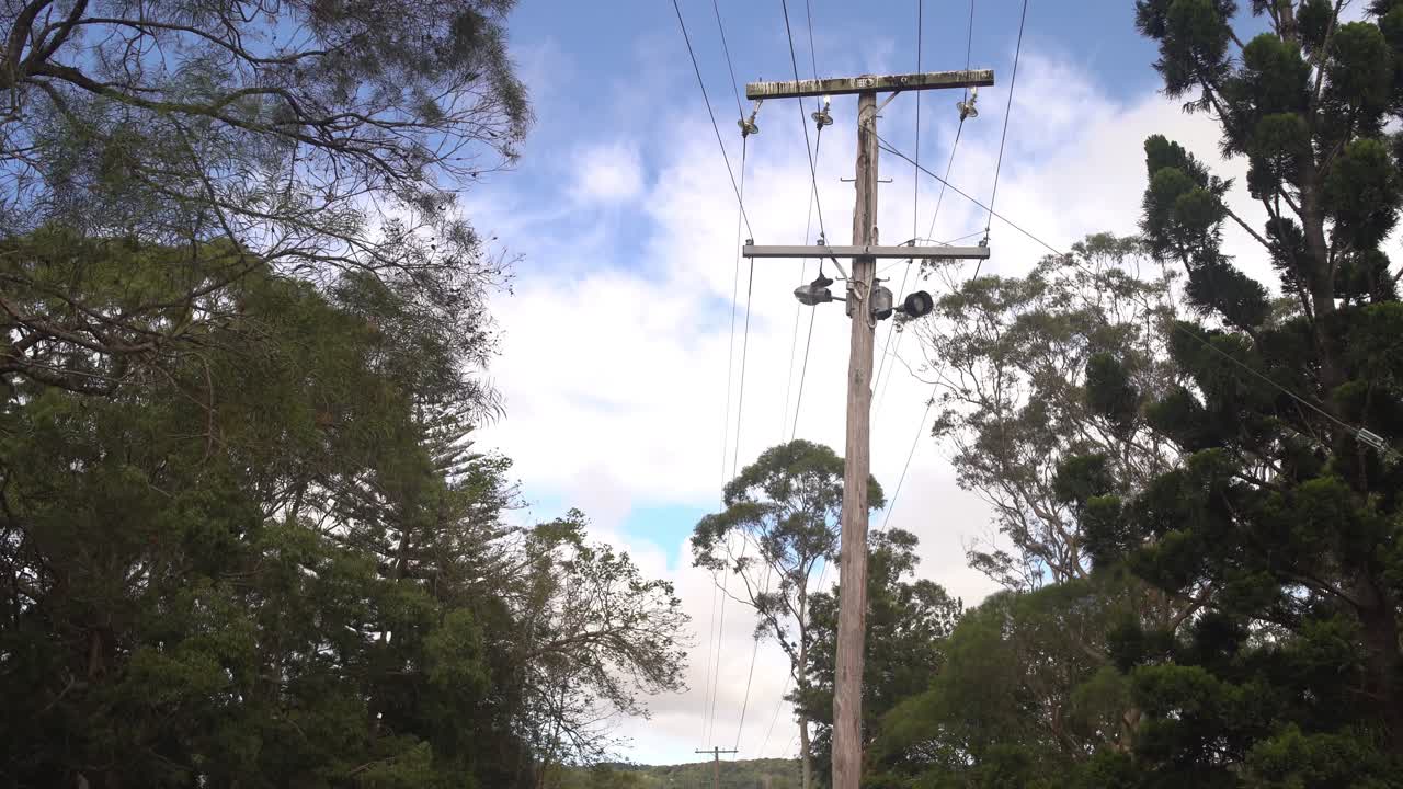 Clouds race across the sky in a timelapse above an old wooden power pole surrounded by trees, evoking a rural and rustic atmosphere.