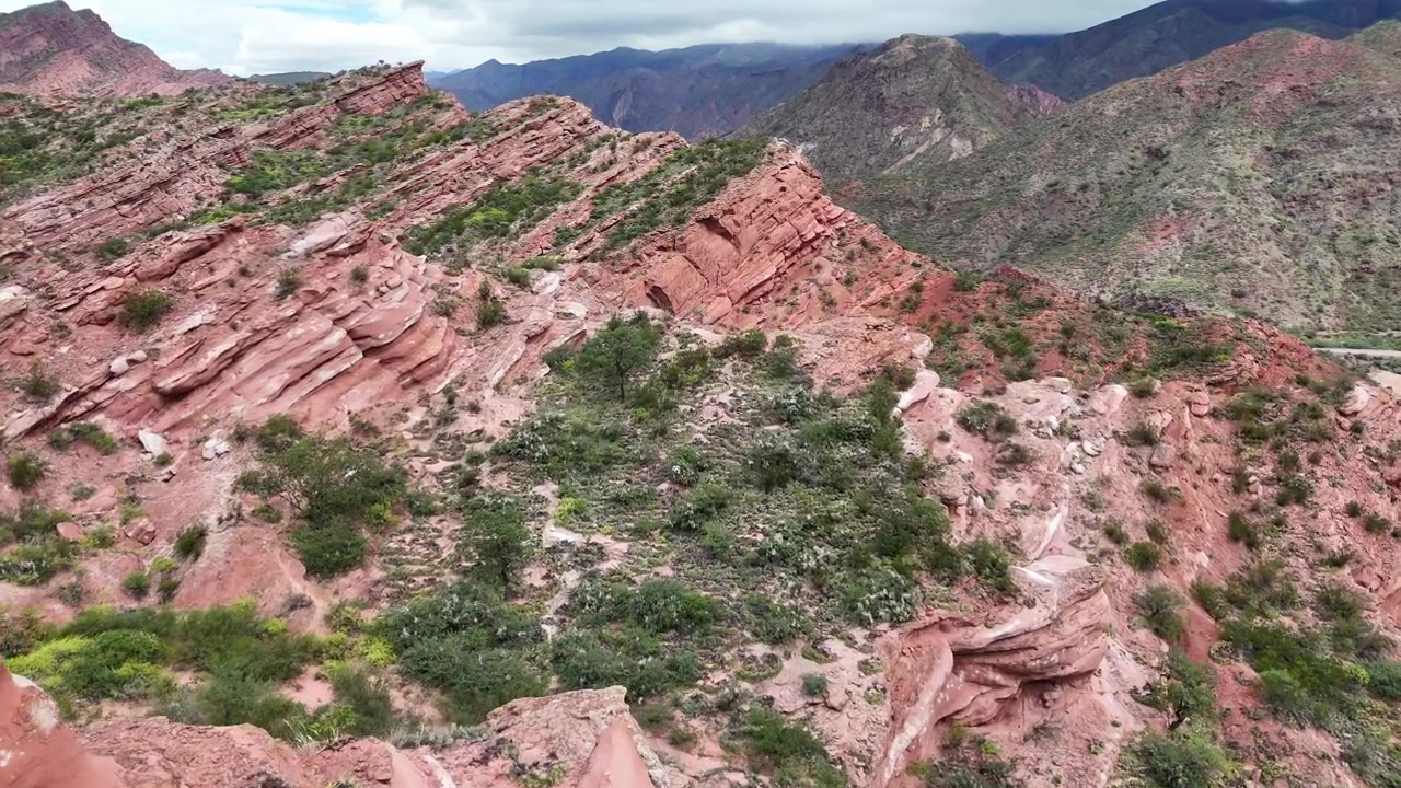 Ripresa aerea con drone di formazioni stratificate di arenaria rossa nella Quebrada de las Conchas, Salta, che mostrano creste frastagliate e terreno desertico creando un paesaggio naturale drammatico