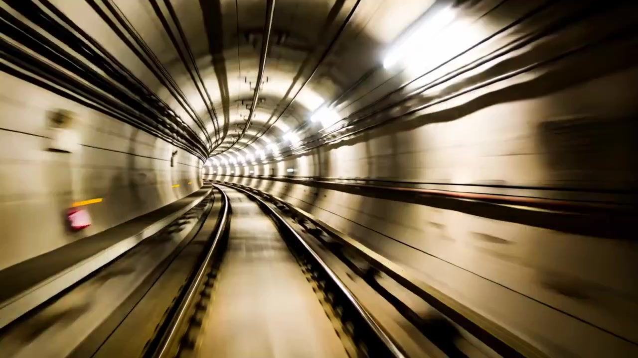 Telecamera di un treno in partenza che riprende un tunnel sotterraneo verso sinistra, mostrando binari convergenti e luci