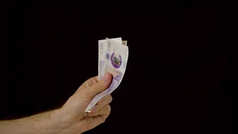 hand rubbing a neat stack of cash money constantly against a black background in slow motion