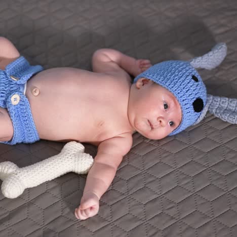 funny costume of a puppy put on a small baby. soft toy bone beside the child. sweet little boy on a grey backdrop