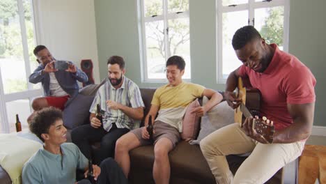 Felices-Amigos-Varones-Diversos-Tocando-La-Guitarra-Y-Hablando-En-La-Sala-De-Estar