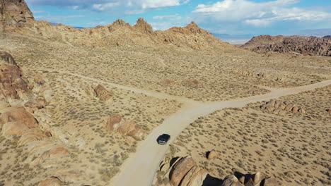 vista aérea de un vehículo furgón oscuro que se desplaza por una carretera desértica en un paisaje seco en un día soleado