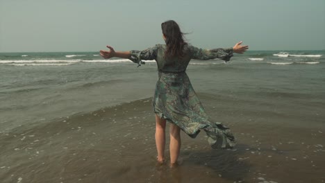 women walking in water along the coastline with wind flowing through her dress