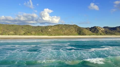 Impresionante-Toma-De-Drones-Flotando-Sobre-Las-Olas-Espumosas-Y-Mirando-Hacia-La-Orilla-De-La-Magnífica-Isla-Fraser