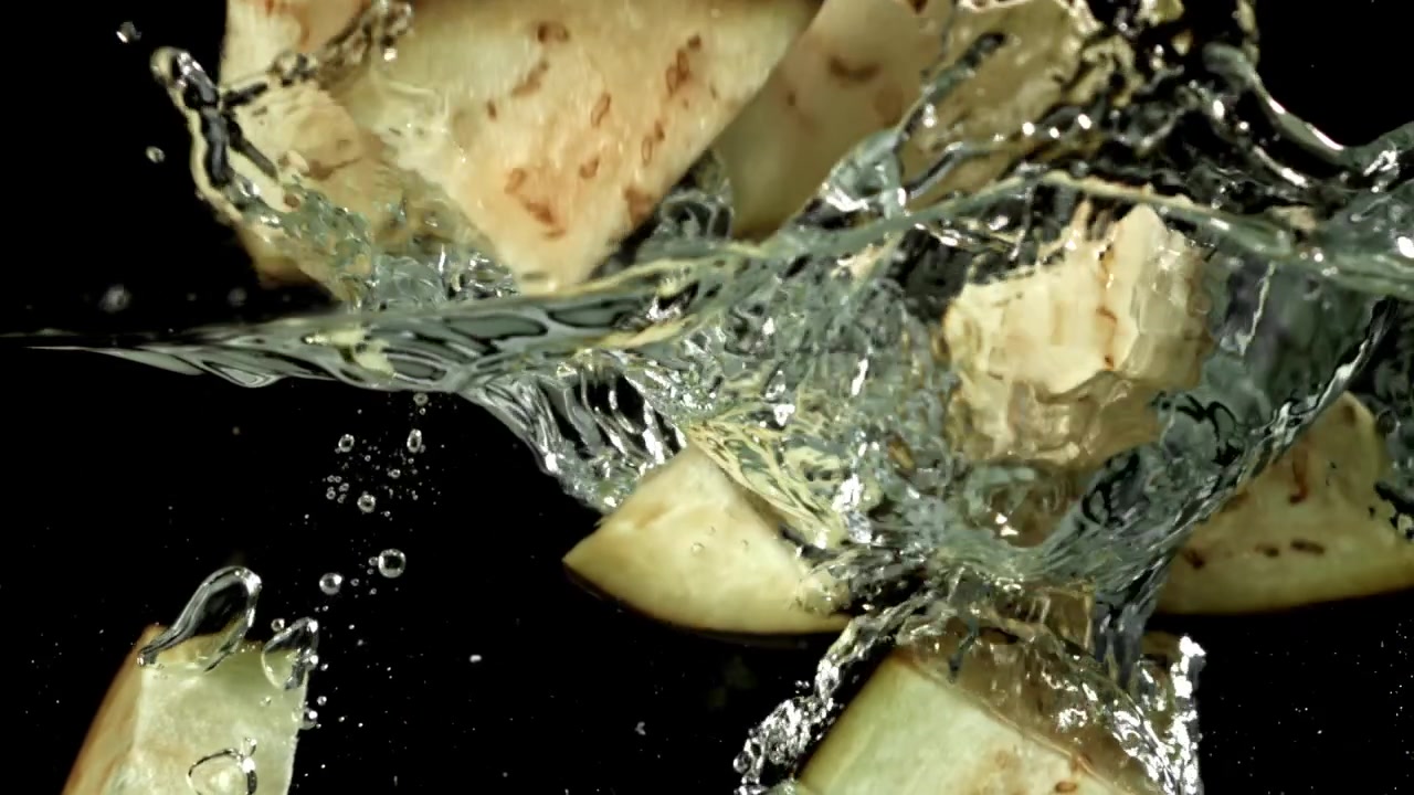 Hakkede aubergine stykker falder ned i vand i slowmotion