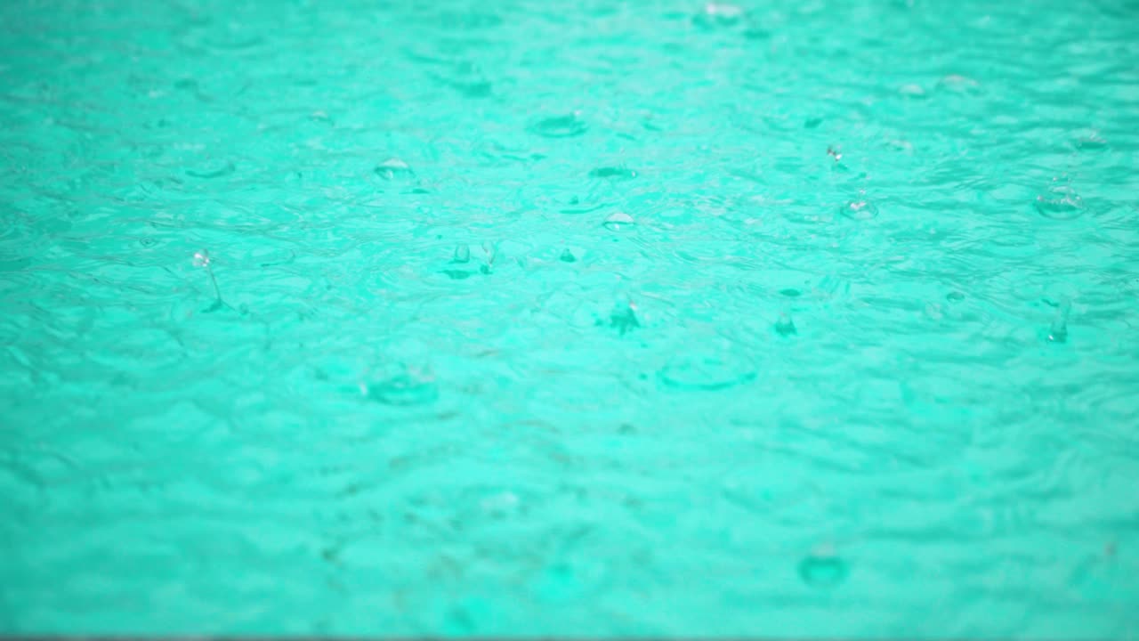 Slow motion close-up of heavy rain hitting pool surface, creating turbulent ripples and waves