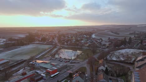 Panoramablick-über-Die-Stadt-Und-Den-Zugefrorenen-See-Mit-Schlittschuhläufern---Drohnenaufnahme