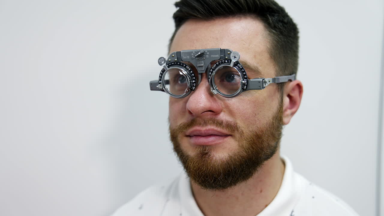 Portrait of a young bearded man in testing glasses. Patient examining his eyesight with optical trial frame in clinic. Ophthalmology concept.