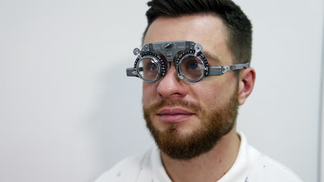 portrait of a young bearded man in testing glasses. patient examining his eyesight with optical trial frame in clinic. ophthalmology concept.