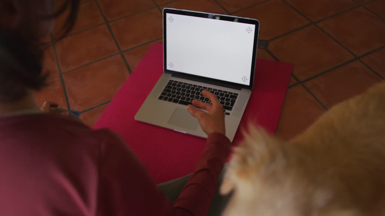 Caucasian woman practicing yoga with her pet dog using laptop with blank screen at home