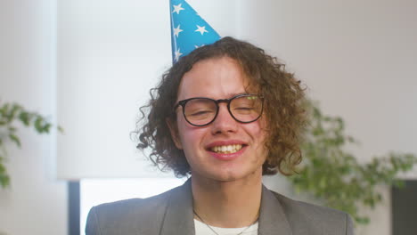 portrait of a happy curly boy with party hat laughing and looking at the camera during a office party